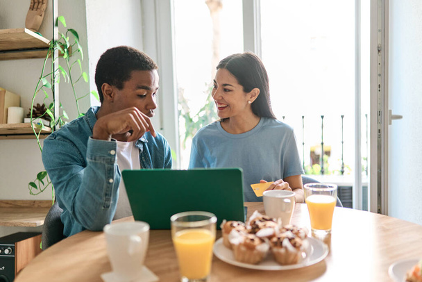 Retrato frontal de um casal multiétnico fazendo compras on-line usando um laptop e cartão de crédito de casa - Foto, Imagem
