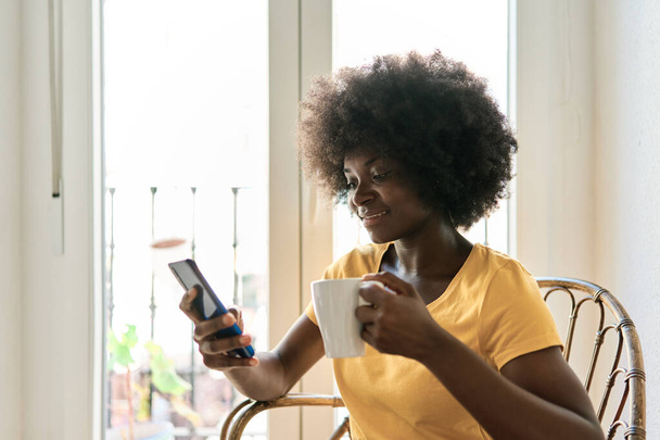 Nahaufnahme Foto einer Frau mit Afro-Frisur mit Handy und Kaffee trinken - Foto, Bild
