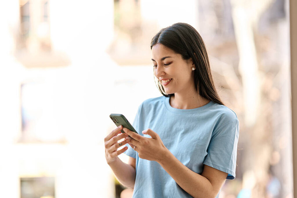 Іспаномовна жінка посміхається, користуючись мобільним телефоном на вулиці - Фото, зображення