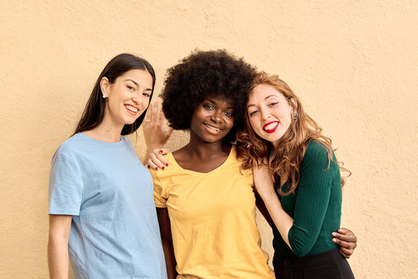 Портрет трех многонациональных подруг, улыбающихся в студии перед камерой - Фото, изображение