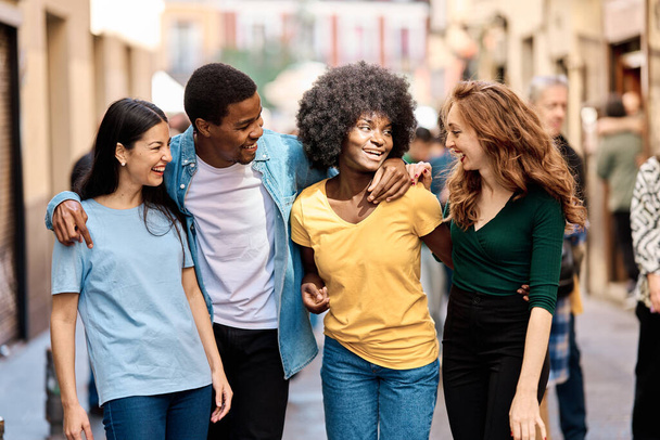 Frontalporträt von vier multiethnischen Freunden, die gemeinsam die Straße entlang gehen - Foto, Bild