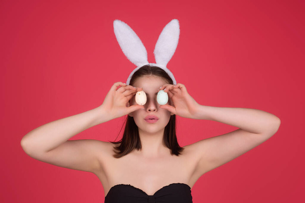 Beautiful young woman with bunny ears and Easter eggs on studio background. Festive bunny and easter eggs season. Stylish woman in Easter bunny ears isolated on studio background - 写真・画像