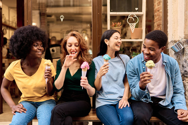 Мультикультурная группа друзей, развлекающихся во время еды мороженого на городской улице - Фото, изображение