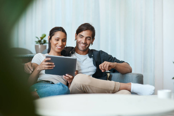 Happy to be watching our favourite show. a young couple sitting on a couch while using a digital tablet at home - Foto, Bild