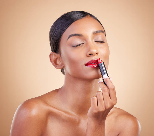Skincare, beauty and woman with lipstick, cosmetics and confident against a brown studio background. Makeup, female and lady with lip gloss, grooming and salon aesthetic with cosmetology and luxury. - Foto, Imagem