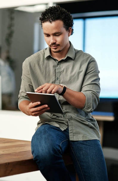 Слежу за нашим прогрессом. красивый молодой бизнесмен, сидящий один в офисе и пользующийся цифровым планшетом - Фото, изображение