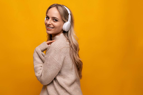 grimaces κορίτσι με μεγάλα ακουστικά σε ένα στούντιο με κίτρινο φόντο. - Φωτογραφία, εικόνα