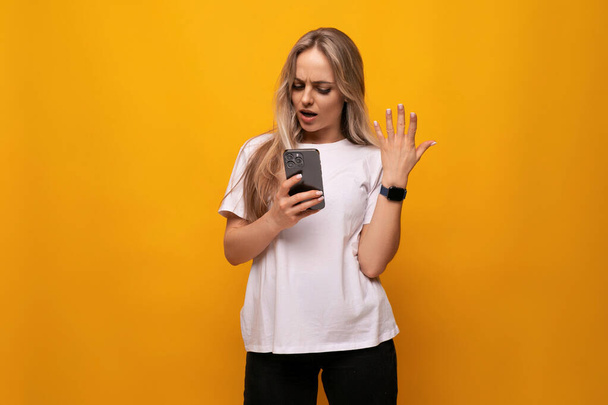 Empörtes Mädchen mit Smartphone in der Hand auf gelbem Hintergrund. - Foto, Bild