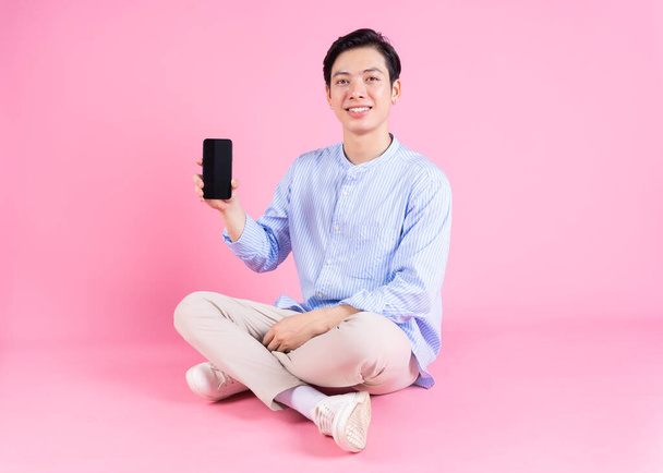 Young Asian man sitting and using smartphone on background - Fotó, kép