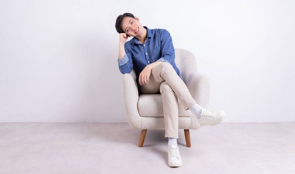 Joven asiático hombre sentado en sillón sobre fondo blanco - Foto, imagen