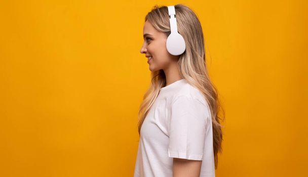 half-turned girl in white headphones on a yellow background with empty space. - Photo, Image