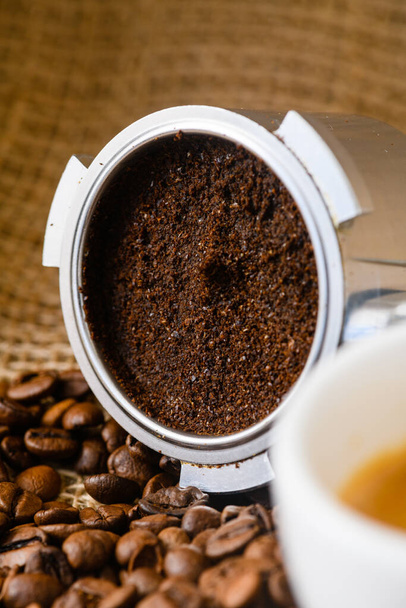 Abgebrannter oder gebrauchter Kaffeesatz mit Portafilter und einer Tasse frisch gebrühtem Kaffee im Hintergrund - Foto, Bild