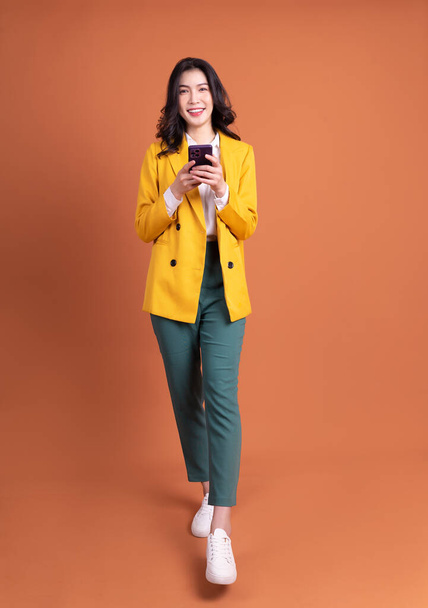 Full length image of young Asian woman using smartphone on background - Foto, afbeelding