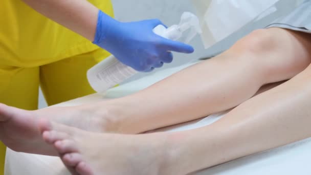Procedimiento de depilación de piernas. El esteticista espolvorea los pies de los clientes con agua, un producto especial. Epilación indolora. - Imágenes, Vídeo