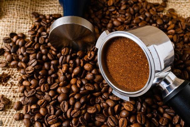 Κοντινό πλάνο macro λεπτή άλεση καφέ για espresso σε μεταλλική βάση για χαρουπιέρα με πλαστογράφηση, κάτοχος και φασόλια, φυσικό υπόβαθρο - Φωτογραφία, εικόνα