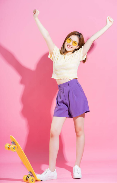 Fénykép ázsiai tizenéves lány gördeszka rózsaszín háttér - Fotó, kép