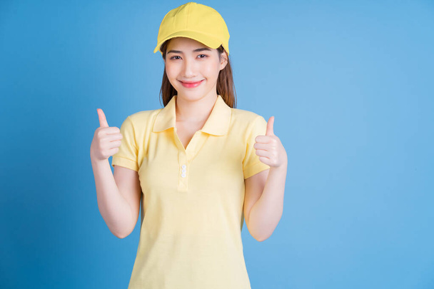 Image of young Asian delivery woman on blue background - Fotó, kép