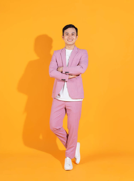 オレンジ色の背景に立つ若いアジア人男性の完全な長さの画像 - 写真・画像