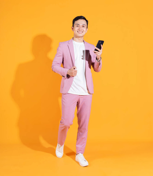 Full length image of young Asian man  standing on orange background - Foto, Imagen