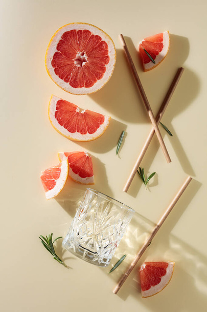 Grapefruit slices, rosemary, straws, and an empty glass. Top view. - 写真・画像