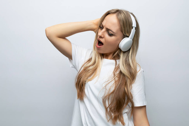 una chica con entusiasmo y alegría en su cara escucha música en grandes auriculares blancos sobre un fondo blanco con espacio vacío. - Foto, Imagen