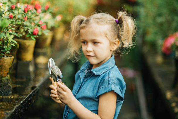 Child planting spring flowers. Little girl gardener plants azalea. Girl holding azalea bush in flower pot. Child taking care of plants. Gardening tools. Copy space - Photo, image