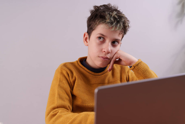 Close-up shot of a young child using a laptop computer. The child appears to be deep in thought, with eyes gazing upwards and head resting on their hand. The laptop screen is visible in the foreground, slightly blurred and out of focus. - Foto, afbeelding