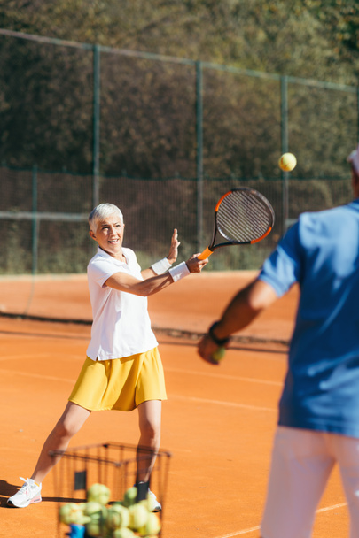 Starsza kobieta ćwiczy tenisa z instruktorem - Zdjęcie, obraz