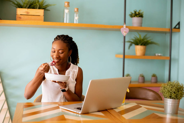 ładna młoda czarna kobieta mając zdrowe śniadanie podczas pracy na laptopie w kawiarni - Zdjęcie, obraz