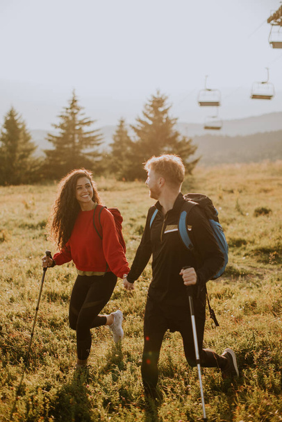 Улыбающаяся молодая пара идет с рюкзаками по зеленым холмам - Фото, изображение