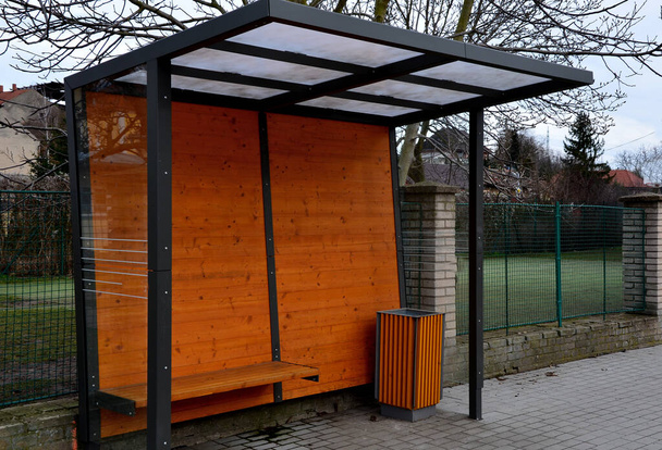 city bus stop. glass shelter with integrated wooden bench. only the roof and the back wall. on the street by the sidewalk in the city. elegant arch, station, platform, lawn, roof, black, frame, seat - Photo, Image