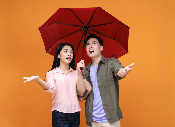Young Asian couple with umbrella on background - Фото, изображение