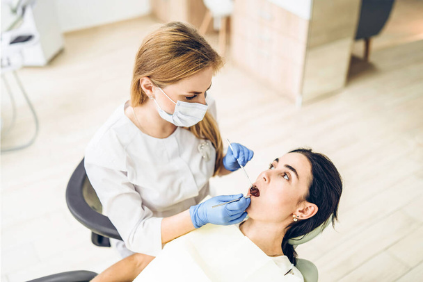 Female dentist with female patient in dental chair providing oral cavity treatment - Fotografie, Obrázek