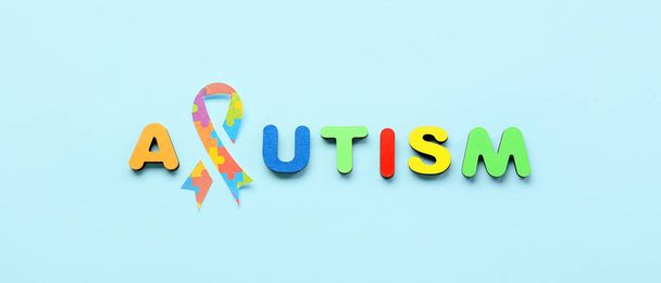 Word AUTISM with paper awareness ribbon on light blue background - Photo, Image