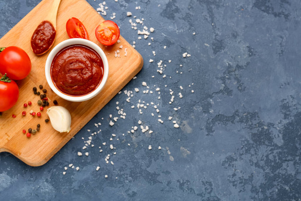Composition with bowl of tasty tomato paste, spoon, peppercorns and salt on blue grunge background - Foto, Bild