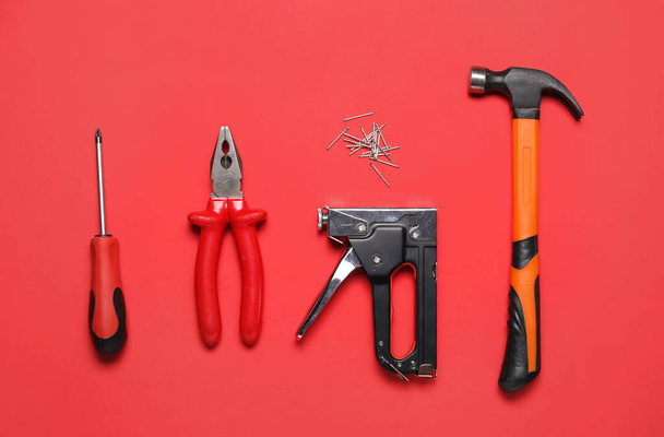 Screwdriver, pliers, building stapler and hammer on red background - Photo, Image