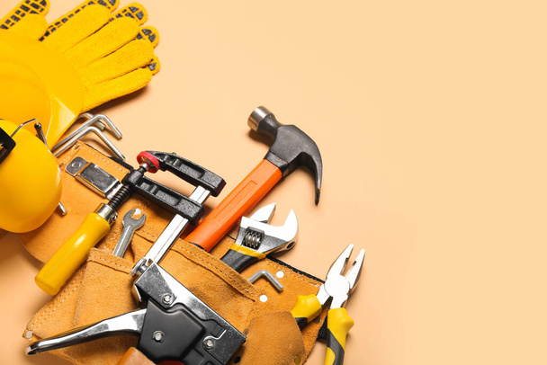 Alicates en cinturón con herramientas y guantes sobre fondo beige - Foto, imagen