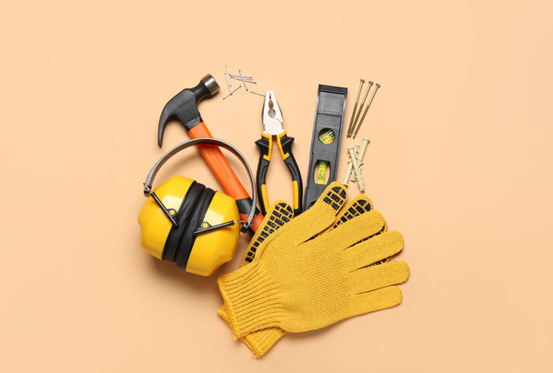 Alicates, martillo, protectores auditivos y guantes sobre fondo beige - Foto, Imagen