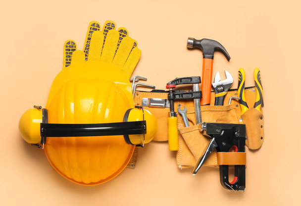 Hardhat, hearing protectors and pliers in belt with tools on beige background - 写真・画像