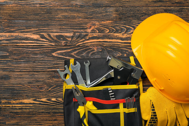 Pliers in tool belt, hardhat and gloves on wooden background - Foto, immagini