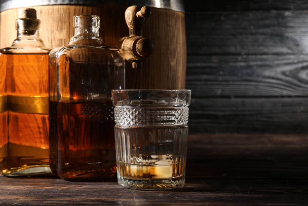 Oak barrel with bottles glass of cold whiskey on dark wooden background - Фото, зображення