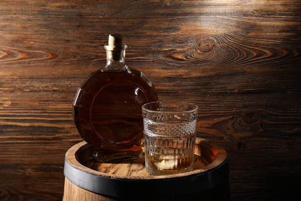 Bottle and glass of cold whiskey on barrel against wooden wooden background - Photo, image