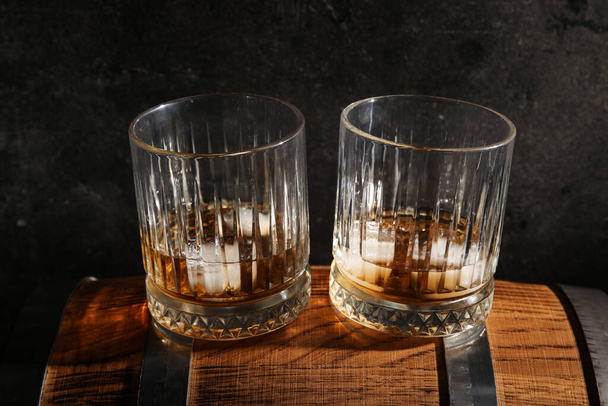 Glasses of cold whiskey on wooden barrel against dark background - Photo, Image