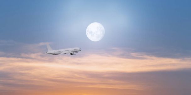 Avión de pasajeros volando al atardecer y luna llena brillando en el fondo. Concepto de turismo, transporte, viajes y carga - Foto, Imagen