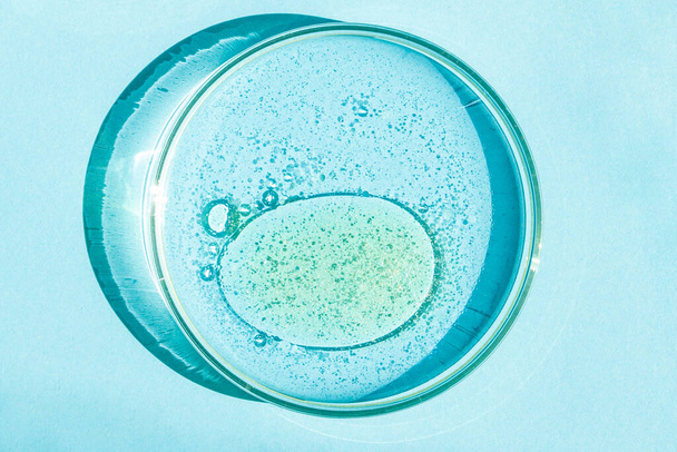 Petriho miska. Petriho pohár s tekutinou. Chemické prvky, olej, kosmetika. Gel, voda, molekuly, viry. Detailní záběr. Na modrém pozadí. - Fotografie, Obrázek