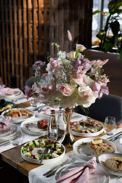 serwowany stół w restauracji ozdobiony jest luksusowym bukietem. Róże ogrodowe, eustoma, populus eukaliptus. pastelowe kolory. - Zdjęcie, obraz