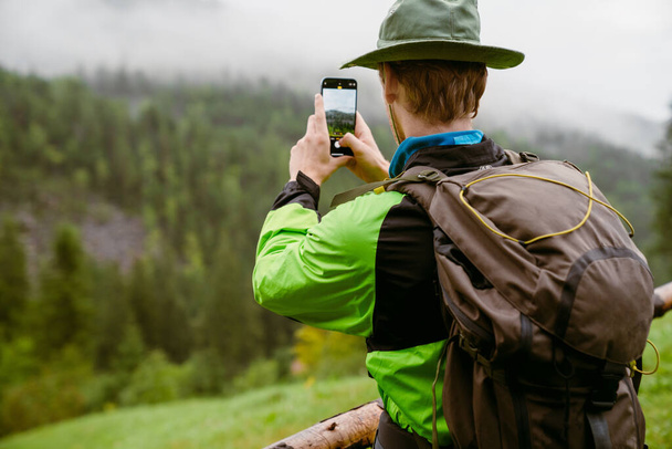 Young white man wearing trekking equipment taking photo of nature while hiking in mountain forest - Foto, Bild