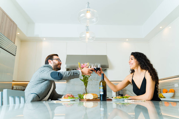 Casal atraente alegre fazendo um brinde enquanto bebe vinho durante seu jantar formal em casa e sorrindo - Foto, Imagem