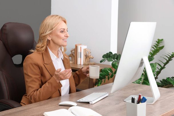 Lady boss with cup of drink near computer at desk in office. Successful businesswoman - Foto, Imagem