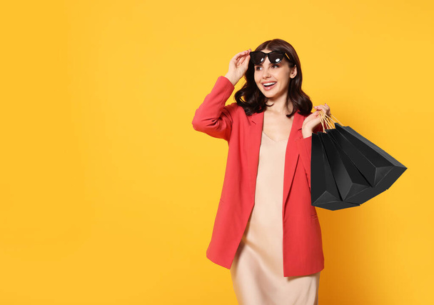Beautiful young woman with paper shopping bags on yellow background. Space for text - Foto, immagini